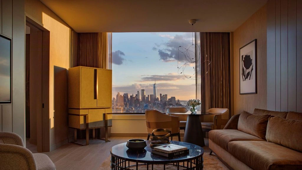 Modern furnished corporate apartment interior with sofa, workspace, and large window overlooking the New York City skyline at sunset.